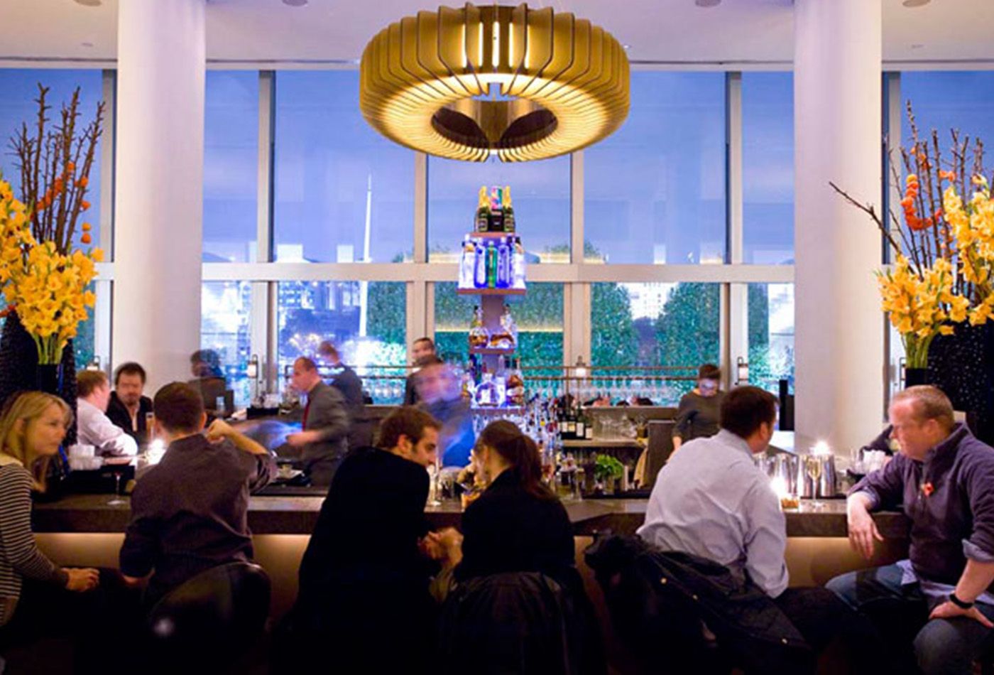 People enjoying a seat at the bar in the evening, large pendant light and views of the city in the background