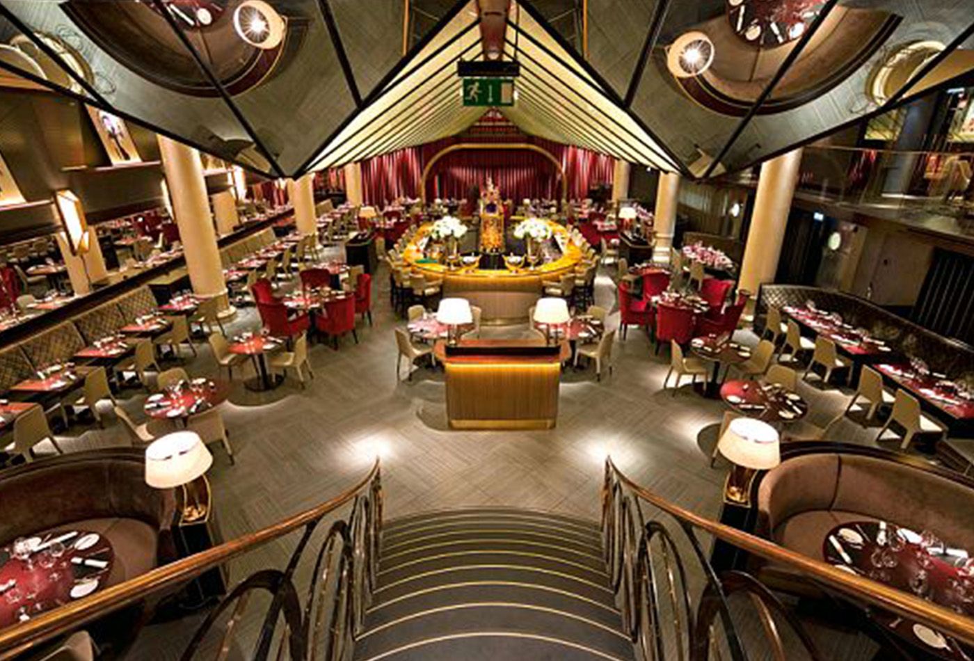 Staircase down to dining area decorated with red fabric chairs and oval bar