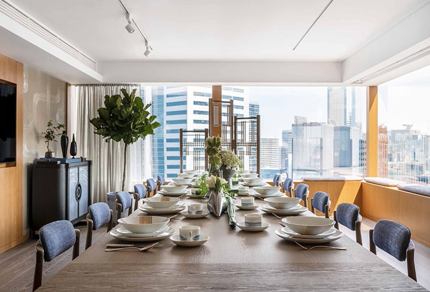 Private room with muted yellow walls, long dining table, windows spanning the width of the room and plants 