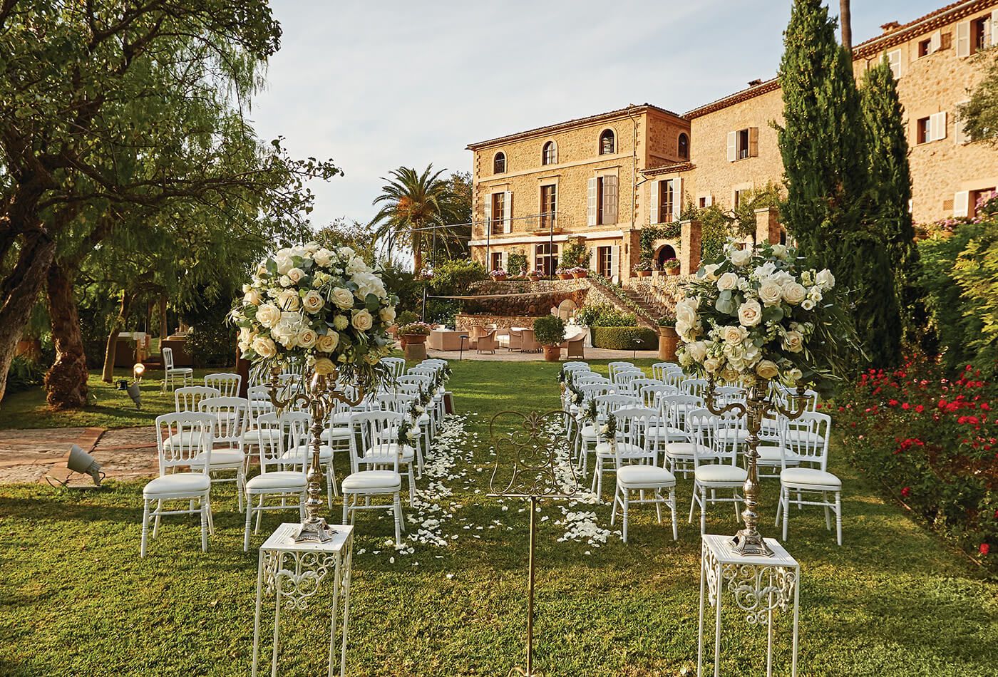 Wedding ceremony in the gardens of the venue, white seating and roses