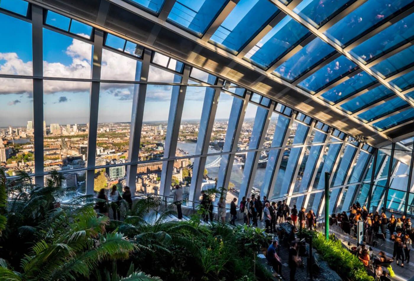 The stairway surrounded by expansive sheets of glass, plants and views of the city.