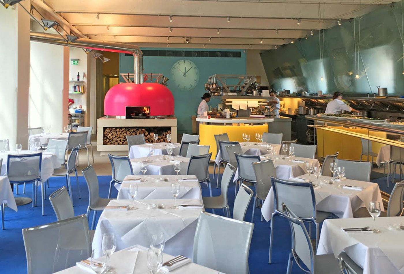 Long, open dining room and kitchen seamlessly roll into one another, accompanied by a long bar facing the floor-to-ceiling windows and pink pizza oven