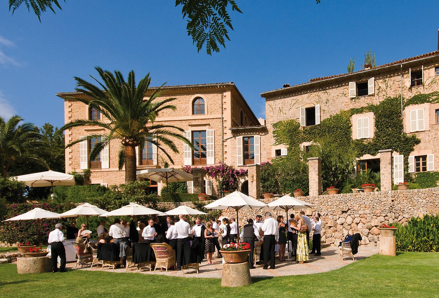 Outdoor wedding reception, guests drinking under sun umbrellas in front of the venue