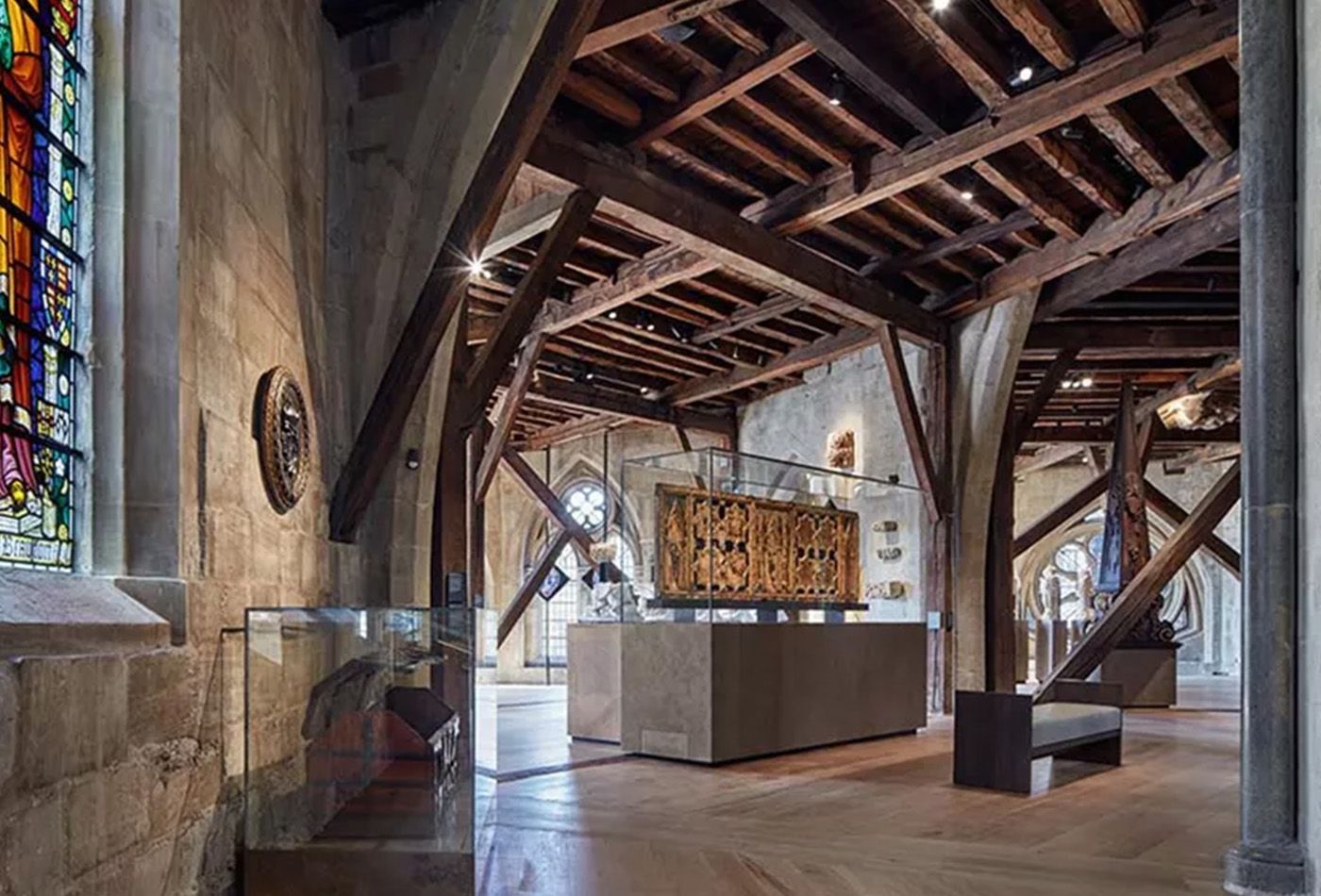 Indoor gallery space with stone walls, wooden beamed ceiling and stained glass windows