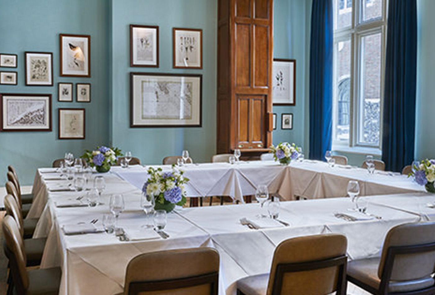 Large square table set up for dining in vast victorian dining room with high ceilings