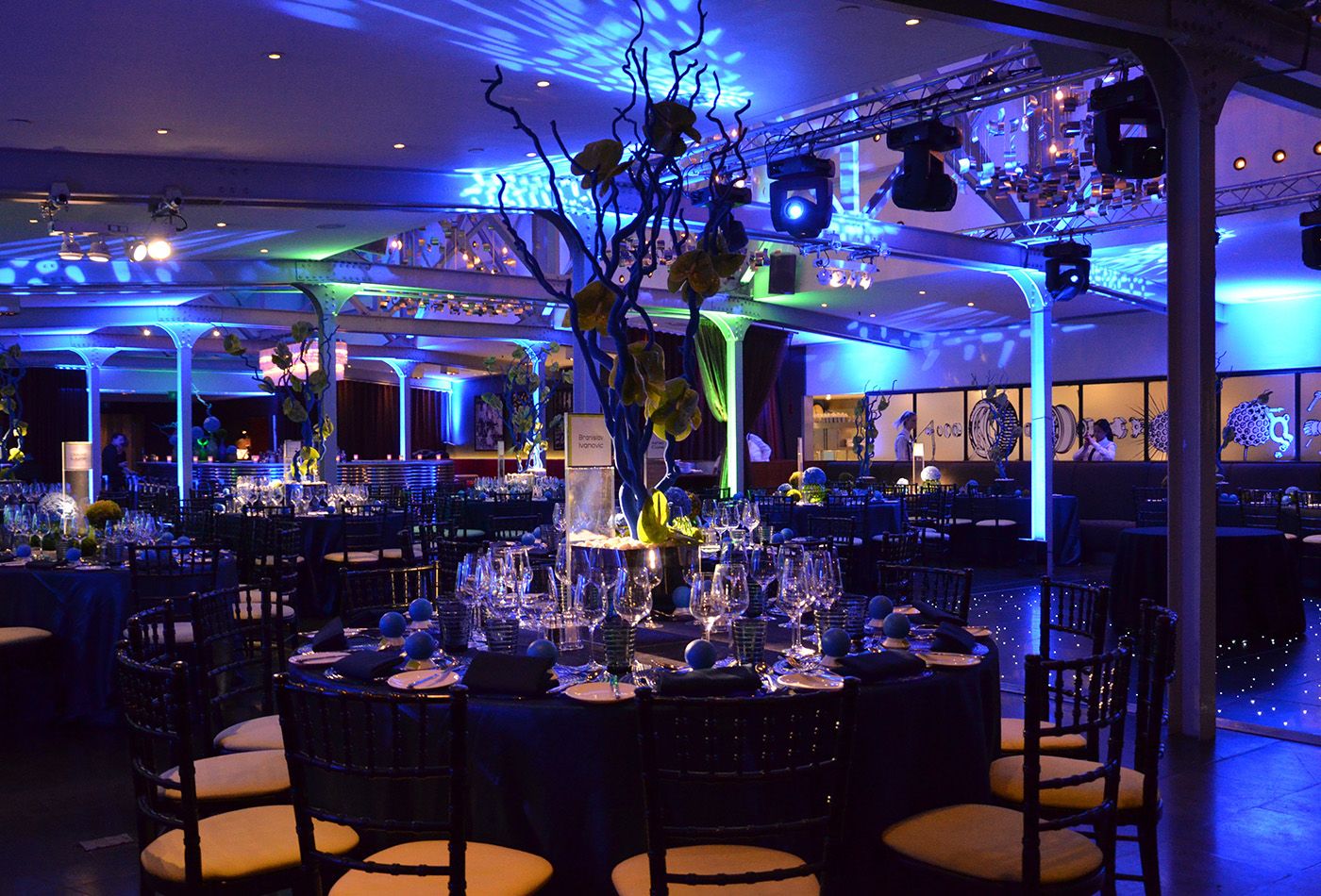 Dark dining space with round tables, leafless trees and moody blue lighting