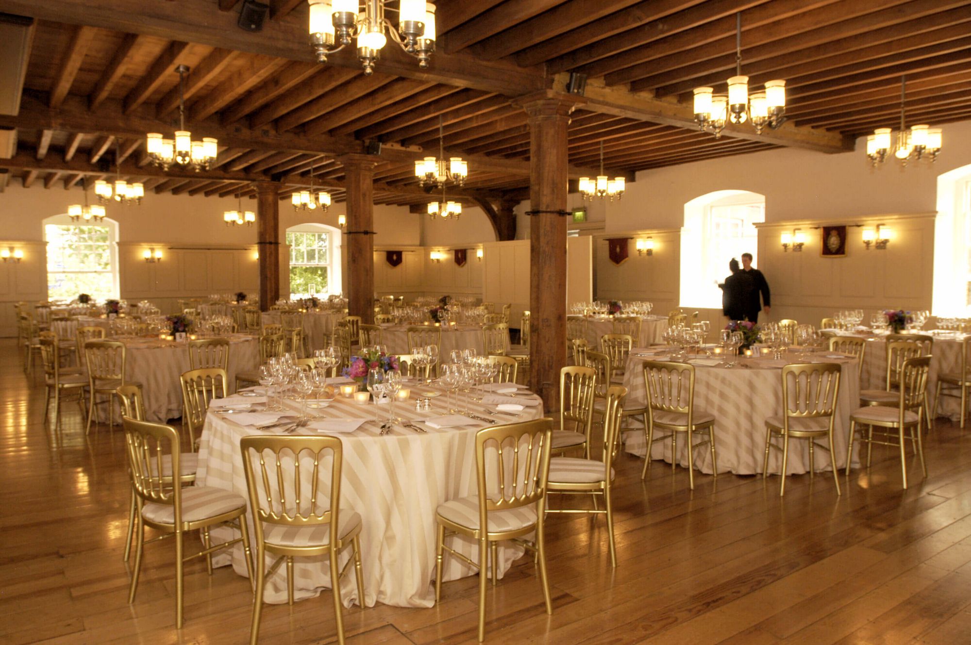 White wedding dining with circular tables, golden chairs and wooden beamed ceiling