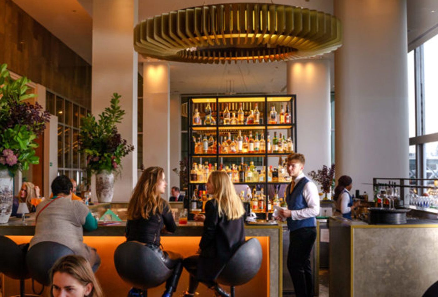 Two women sitting at the Skylon bar, themes of orange, green and gold