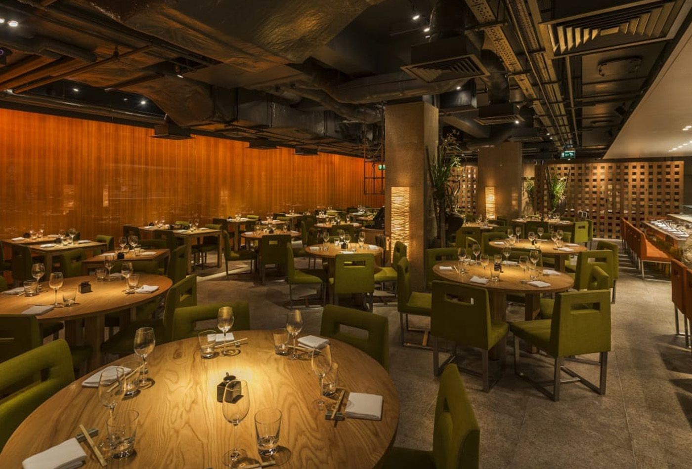 Modern restaurant made up of round tables, wooden feature wall and green fabric chairs